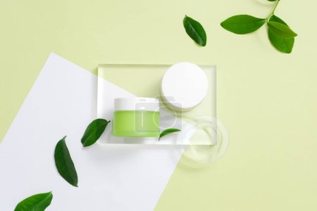 Photo for Two jars of lotion are placed on a rectangular glass platform, fresh green tea leaves are randomly arranged on a minimalist background. Beauty theme. Flat lay. - Royalty Free Image
