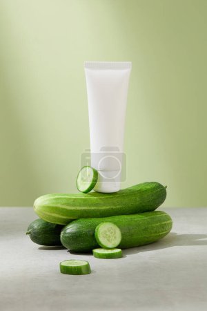 Photo for Front view of the unlabeled cleanser tube is placed on top of cucumbers, with a few fresh cucumber slices decorated next to it. Mockup for vegan cosmetics advertisement. - Royalty Free Image
