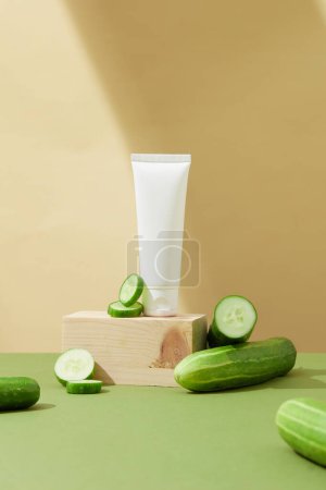 Photo for Front view of unlabeled white cream tube displayed on a podium and fresh cucumbers on a pastel background. The pantothenic acid (vitamin B5) content in cucumbers helps treat acne. - Royalty Free Image