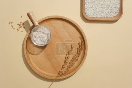 Photo for White rice is stored in a square wooden tray, rice flour is stored in a glass bowl on a round wooden tray. Minimalist beige background suitable for cosmetics advertising. - Royalty Free Image