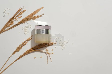 Photo for A lotion jar with a luxurious design that stands out on a white background with whole grain rice. Rice bran powder contains large amounts of Vitamin B1, which has the effect of making the skin bright. - Royalty Free Image