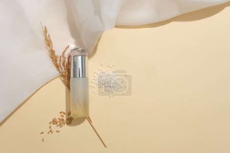 Foto de Arroz integral y un frasco cosmético se muestran juntos sobre un fondo beige. Salvado de arroz contiene altos niveles de vitaminas y minerales, proporcionando muchos ingredientes nutricionales. - Imagen libre de derechos