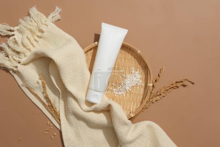 Photo for Close-up of an unbranded cosmetic tube and white rice on a flat winnowing basket on a brown background. Cosmetics contain natural ingredients. Top view. - Royalty Free Image