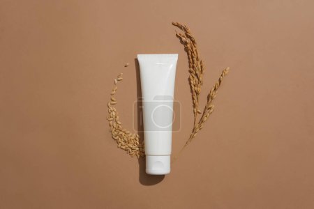 Photo for An unlabeled lotion tube and whole grain rice on a brown background. Rice bran extract contains many nutrients and antioxidants that help brighten skin and limit melasma. - Royalty Free Image