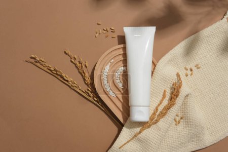 Photo for A plastic tube and rice are displayed on a domed platform next to a beige cloth on a brown background. Blank label for lettering design. Vegan cosmetics with rice bran extract. - Royalty Free Image