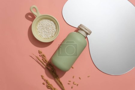 Photo for A pastel green cosmetics bottle, bean-shaped mirror, and rice on a pink background with a ceramic dish. Perfect space for advertising and showcasing beauty essentials. - Royalty Free Image
