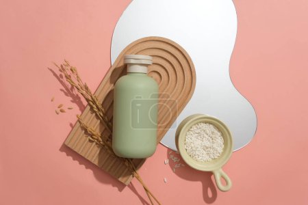 Photo for On a pink background there is a pastel green cosmetics bottle, a bean-shaped mirror, a dome-shaped platform and rice served in a ceramic dish. Space for advertising. - Royalty Free Image