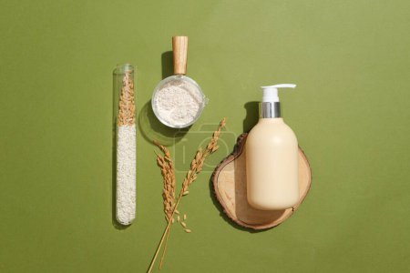 Photo for Unlabeled shower gel bottle on a log, rice flour in a glass bowl, and whole grain rice in a test tube against a moss green backdrop. Perfect ad space. - Royalty Free Image