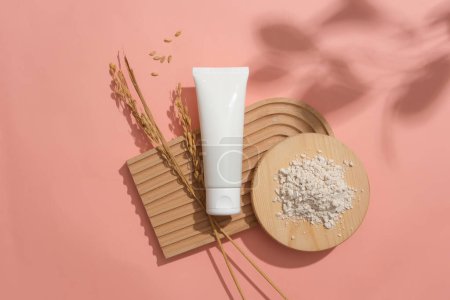 Photo for Rice bran powder is displayed on a round wooden podium. An unlabeled white tube and rice are placed on a dome-shaped platform on a pink background. Cosmetic ads with natural ingredients. - Royalty Free Image