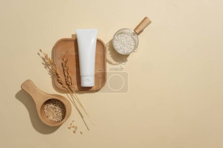 Photo for Top view of an unbranded cosmetic tube is displayed on a wooden tray, rice bran stored in small bowls on a beige background. Blank space for advertising. - Royalty Free Image