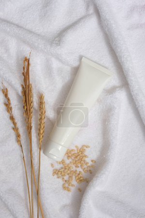 Photo for White towel decorated as a background with wheat ears, wheat seeds and unbranded tube displayed on. Natural skin care concept with empty label - Royalty Free Image