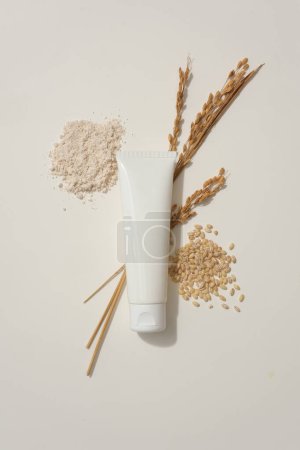 Téléchargez les photos : Une poignée de son de riz et de graines de blé sont disposées sur fond blanc. Tube sans marque et oreilles de blé affichées. Emballage de récipient de marque de soins de la peau - en image libre de droit
