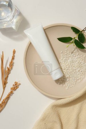 Foto de Plato redondo con un tubo de belleza con arroz y hojas verdes. Dispuesto con una toalla, espigas de trigo y un vaso de agua. Tubos de burla para el cuidado de la piel cosmética - Imagen libre de derechos