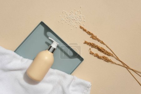 Photo for Beige background featured a tray with unbranded pump bottle and white towel displayed on. Rice bran powder not only decongests pores, but also can brighten - Royalty Free Image