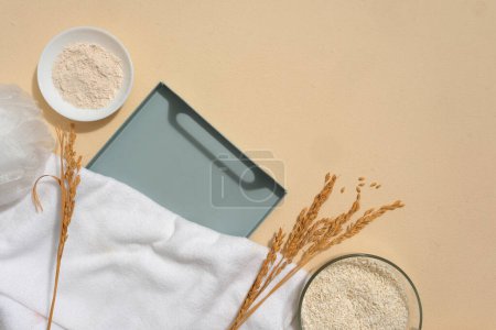 Photo for A tray arranged with wheat ears, a towel, a dish of rice bran and a bowl containing rice. Beige background. Vacant space on the tray to show organic products - Royalty Free Image