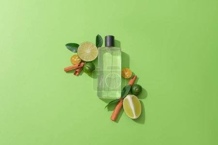 Foto de Una botella de perfume transparente se muestra con kumquat, limón y canela sobre un fondo verde. Maqueta cosmética para publicidad. Olor a hierbas. - Imagen libre de derechos