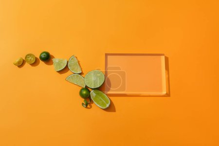 Téléchargez les photos : Le kumquat frais et le citron sont placés à côté d'une plate-forme en verre transparent sur un fond orange. Espace idéal pour l'affichage des produits. Concept d'ingrédients naturels. - en image libre de droit