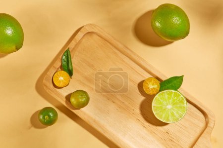 Téléchargez les photos : Plateau rectangulaire en bois, citrons et kumquats sur fond couleur peau. Citrons fournissent beaucoup de vitamine C, fibres et divers composés végétaux bénéfiques. - en image libre de droit