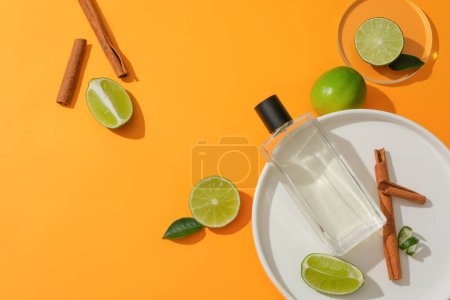 Foto de Frasco de perfume transparente en un plato blanco con canela, limón y kumquat sobre un fondo vibrante. Delicada fragancia vegetal. Espacio de copia para anuncios cautivadores. - Imagen libre de derechos