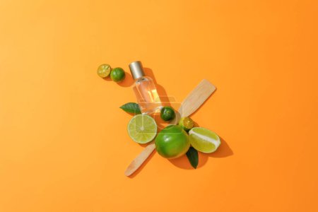 Foto de Vista superior de un frasco cosmético transparente, limón fresco, kumquat y cuchara de madera colocados uno al lado del otro sobre un fondo naranja. La vitamina C se encuentra en la fruta fresca. - Imagen libre de derechos
