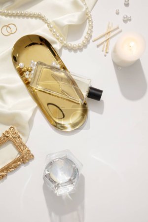 Photo for Fashion composition with accessories on white background. Pearl necklace, ring, scented candle and fabric decorated. A glass perfume bottle unlabeled displayed on gold tray. Mockup for design - Royalty Free Image