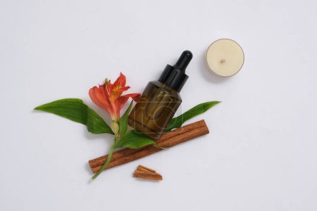 Photo for On a white background, a dropper bottle container essential oil decorated with blooming twig, cinnamon sticks and candle. Minimal concept for advertising. Aromatherapy, wellness, beauty background - Royalty Free Image