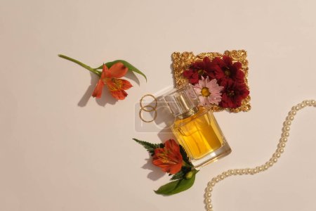 Foto de Fotos publicitarias para productos de perfumes de mujeres. La botella de perfume maqueta está decorada con flores fragantes, un collar de perlas y anillos sobre fondo beige. Producto de cuidado de belleza botánica - Imagen libre de derechos