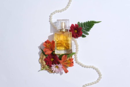Foto de Concepto simple pero elegante para un perfume de publicidad femenina. Una botella de vidrio sin etiqueta con hermosas flores, hoja de helecho y collar de perlas decoradas sobre fondo blanco - Imagen libre de derechos