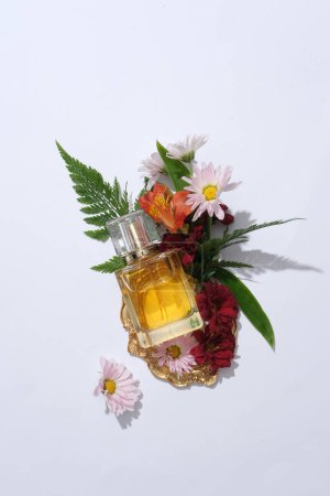 Photo for Top view of perfume bottle unbranded displayed with fresh beautiful flowers and green leaves on a white background. Mockup for design and advertising scene. Aromatherapy, wellness, beauty background - Royalty Free Image