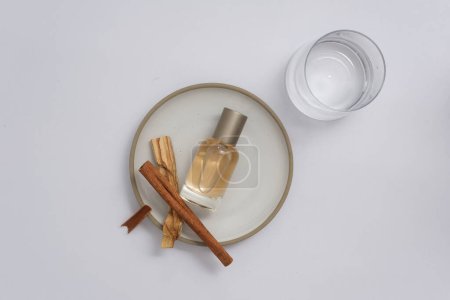 Foto de Producto de aromaterapia herbal, escena publicitaria con frasco de perfume sin etiquetar decorado con palitos de canela sobre fondo blanco. Vista superior, aceite esencial de canela - Imagen libre de derechos