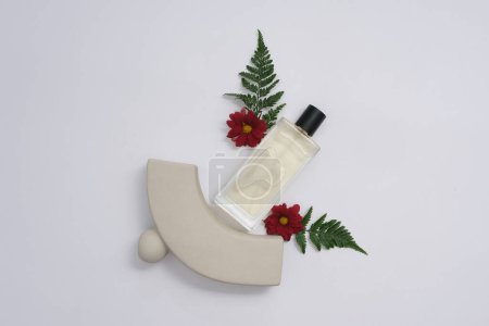 Téléchargez les photos : Concept d'aromathérapie botanique avec maquette de bouteille en verre décorée sur fond blanc. Fleurs rouges fraîches et fougères se détachent contre le vase gris exposé. Vue d'en haut, espace design - en image libre de droit