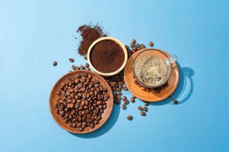 Foto de Granos de café en un plato de madera, café en polvo en un tazón de madera y una taza de café negro que sobresale sobre un fondo azul. El café trae muchos beneficios para el cuerpo. - Imagen libre de derechos