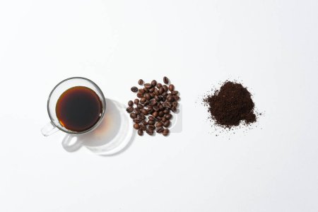 Foto de Una taza de café negro, granos de café y café en polvo dispuestos cuidadosamente sobre un fondo blanco. Beber café es eficaz para prevenir y reducir el riesgo de ciertas enfermedades. - Imagen libre de derechos