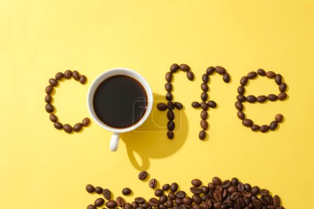 Téléchargez les photos : Les grains de café sont disposés dans le mot COFFE avec une tasse de café noire sur un fond jaune. Images créatives pour la publicité. Espace de copie. Thème café. - en image libre de droit