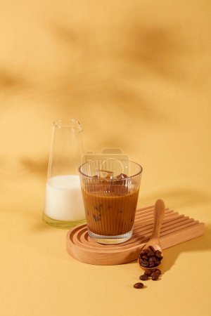 Foto de Un vaso de café con leche y una cuchara de madera con granos de café se muestran en una plataforma de madera. La cafeína en el café tiene la capacidad de quemar grasa y apoyar eficazmente la pérdida de peso. - Imagen libre de derechos