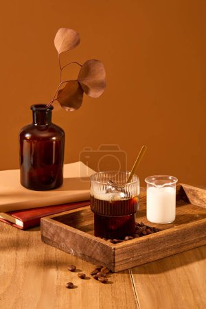 Téléchargez les photos : Les feuilles d'automne sont insérées dans un vase brun, sur un plateau en bois, il y a une tasse de café et une tasse de lait, des grains de café éparpillés sur la table en bois. Espace pour la publicité de café. - en image libre de droit