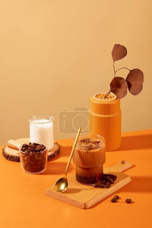 Foto de Taza de café con leche y granos de café sobre tabla de cortar de madera, rodeada de accesorios con fondo marrón anaranjado. Los granos de café tienen muchos beneficios para la salud. - Imagen libre de derechos