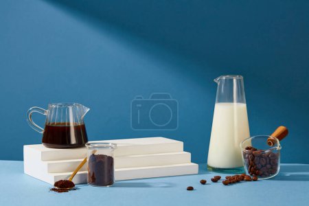 Foto de El café negro, la leche fresca, el café en polvo, el podio blanco y los granos de café se muestran sobre un fondo azul. El café también actúa como un exfoliante para ayudar a reducir el envejecimiento prematuro de la piel. - Imagen libre de derechos