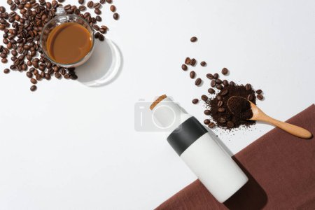 Foto de Un vaso de café con leche, granos de café, termo, café en polvo y una cuchara de madera se colocan sobre un fondo minimalista. Beber café ayuda a perder peso. - Imagen libre de derechos