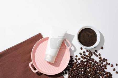 Photo for Top view of a cosmetic tube without label on pink tray, coffee powder in ceramic bowl and coffee beans on white background. Space for cosmetic advertising with coffee extract. - Royalty Free Image
