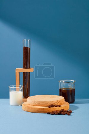 Foto de La plataforma de madera se coloca en el centro del marco, junto a ella hay una taza de leche, una taza de café negro, granos de café y polvo de café en un tubo de ensayo con un fondo azul. - Imagen libre de derechos