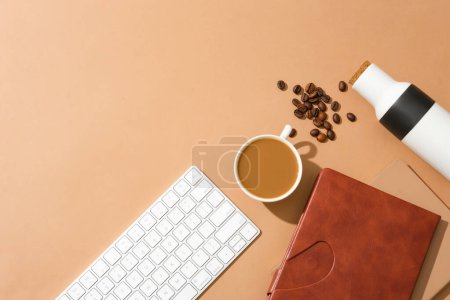 Téléchargez les photos : Une tasse de café laiteux, un clavier d'ordinateur, un cahier, des grains de café et un thermos sont placés sur un fond brun. Avantages du café. Espace pour annonces. - en image libre de droit