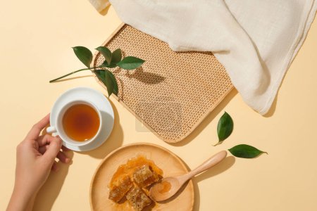 Foto de Plato redondo de madera con cubos de cera de abeja. Modelo de mano sosteniendo una taza de té. Bandeja de bambú con espacio en blanco para la promoción del producto - Imagen libre de derechos