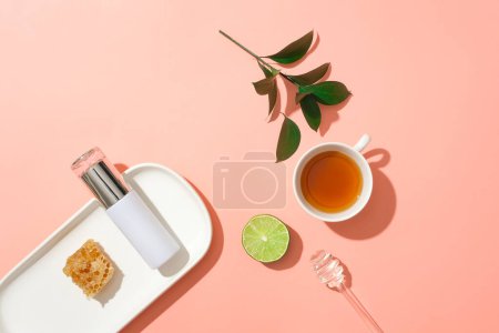 Foto de Un plato con una botella cosmética y cera de abejas. Se muestra una taza de té, rodaja de lima y goteo de miel. La miel es una sustancia pegajosa y dulce - Imagen libre de derechos