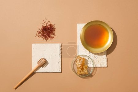 Foto de Un puñado de azafrán, miel goteando, un tazón dorado de miel y una placa de Petri de vidrio de cera de abeja. Fondo beige. La miel ayuda a aliviar la tos en los niños - Imagen libre de derechos