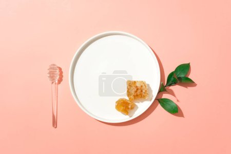 Téléchargez les photos : Vue de dessus d'un plat en céramique avec de la cire d'abeille posée dessus, décoré d'un miel qui dégouline et de quelques feuilles. Le miel est un antiseptique naturel et anti-inflammatoire - en image libre de droit