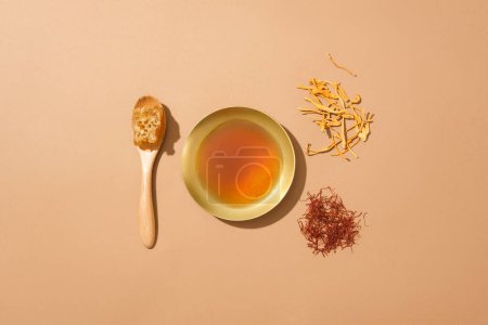Foto de Un plato dorado en forma redonda que contiene miel, arreglado con una cuchara de cera de abeja y un puñado de cordyceps y azafrán. Concepto sanitario - Imagen libre de derechos