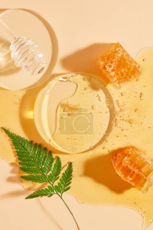 Téléchargez les photos : Podium en verre disposé avec un miel égouttant et de la cire d'abeille sur le miel. Vitrine sur piédestal avec fond beige - en image libre de droit