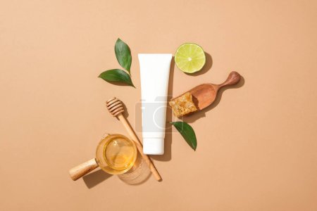 Photo for Blank label tube in white color displayed with glass bowl of honey and beeswax. A honey dripping, leaves and a slice of lime featured. Branding mockup design - Royalty Free Image