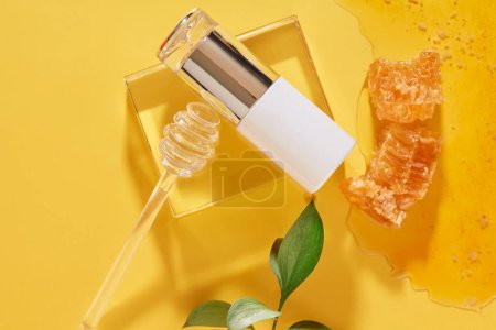Téléchargez les photos : Bouteille cosmétique ornée d'un miel dégoulinant sur un podium en verre. Miel et cire d'abeille sur fond jaune. Image de marque de l'extrait de miel - en image libre de droit